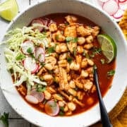 A bowl of easy chicken pozole topped with shredded cabbage, thinly sliced radishes, Mexican oregano, chopped cilantro, and lime wedges.