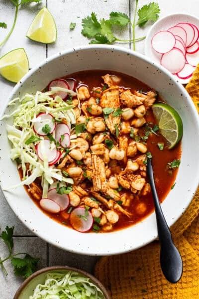A bowl of easy chicken pozole topped with shredded cabbage, thinly sliced radishes, Mexican oregano, chopped cilantro, and lime wedges.
