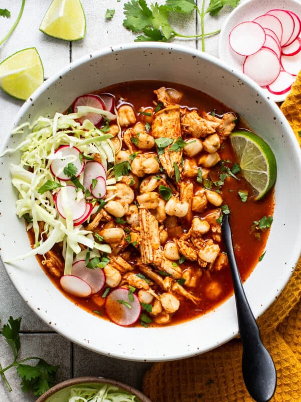 A bowl of easy chicken pozole topped with shredded cabbage, thinly sliced radishes, Mexican oregano, chopped cilantro, and lime wedges.