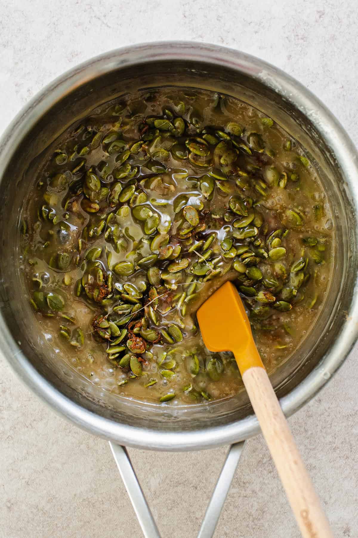 Corn syrup, maple syrup, spices, and roasted pepitas in a pot being mixed together.