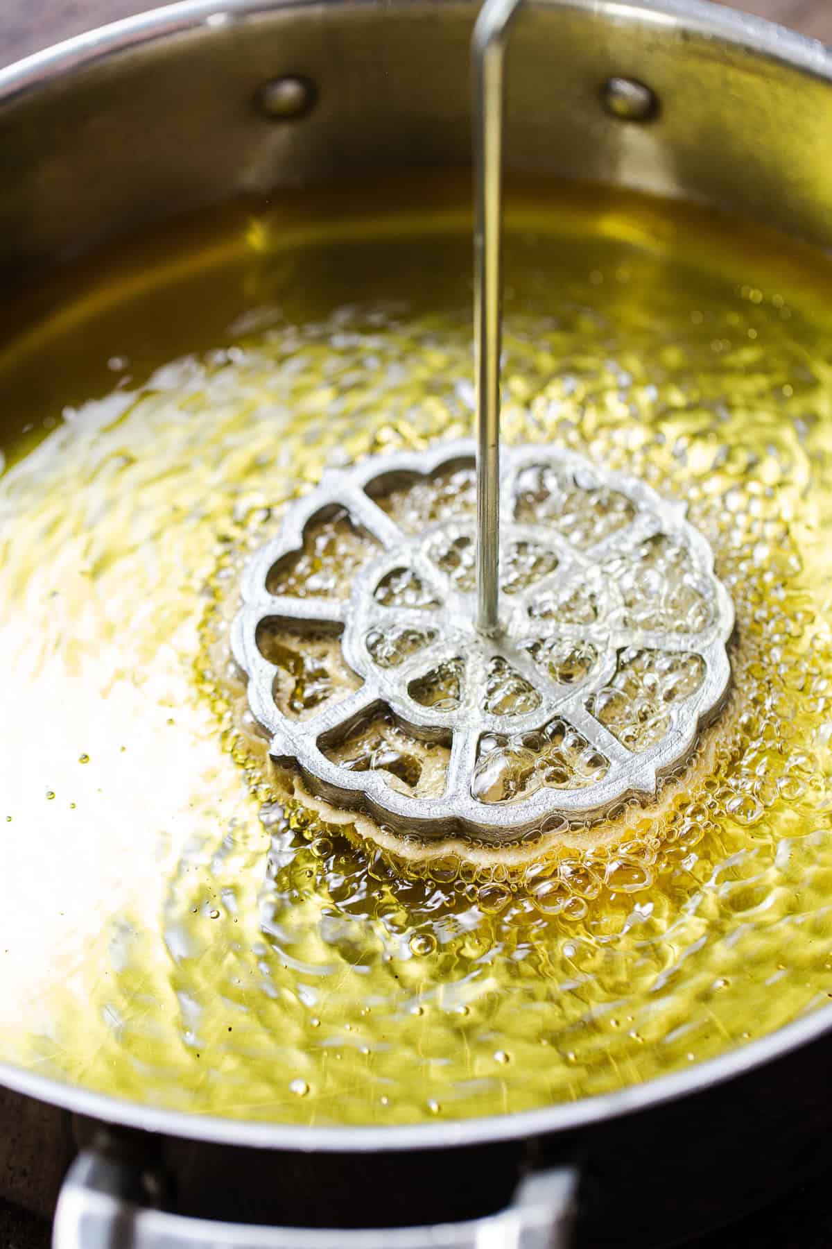 A rosette mold with batter for pumpkin buñuelos in hot oil.