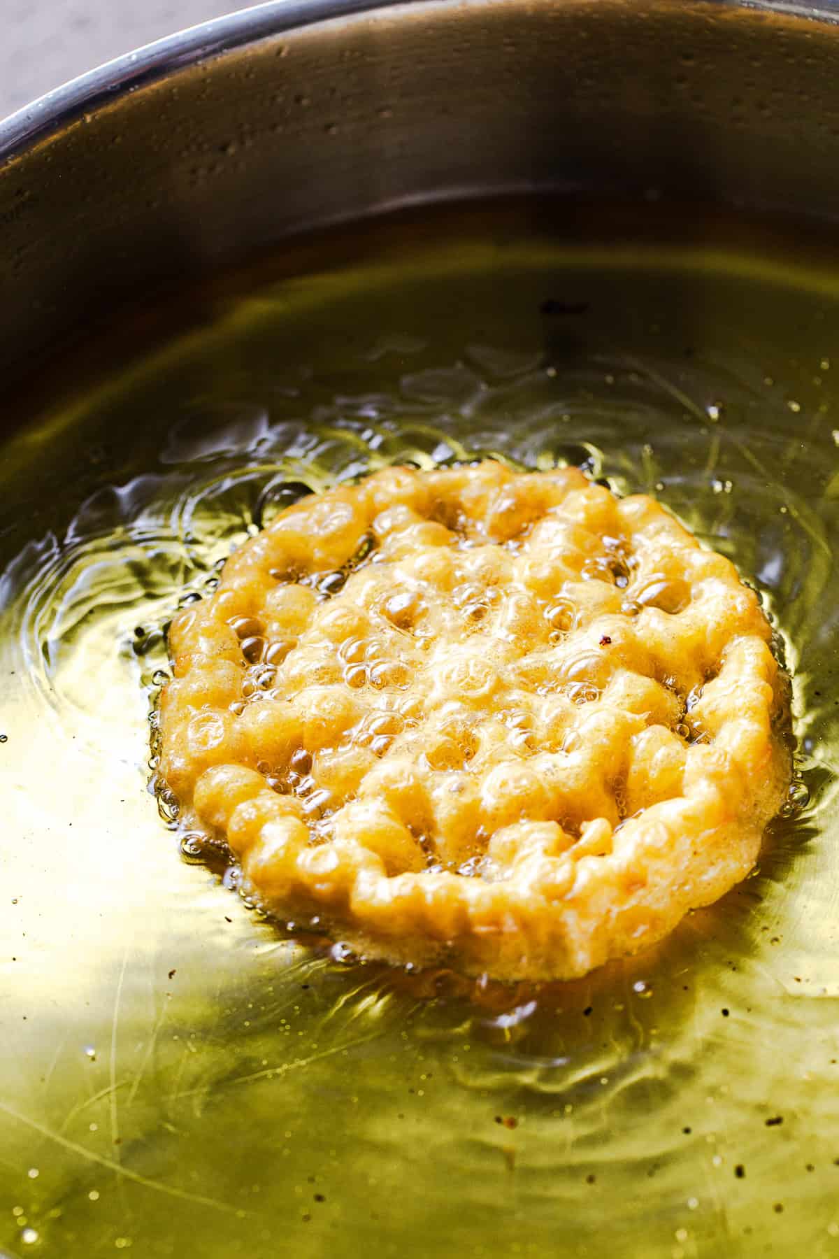 A pumpkin buñuelo de viento being fried in hot oil in a saute pan.