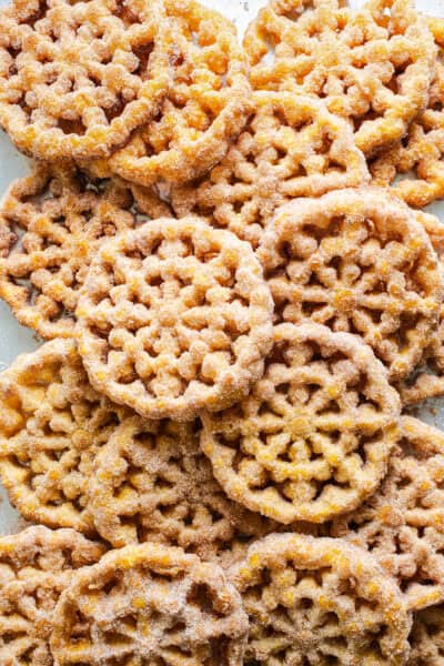 Buñuelos covered in cinnamon sugar on a baking sheet lined with paper towels.