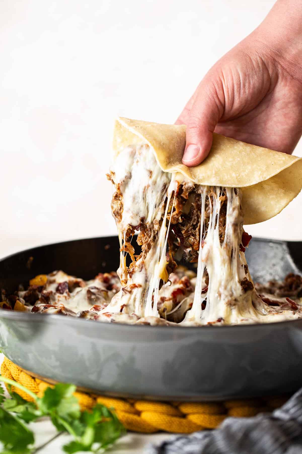 A corn tortilla scooping some filling from the skillet of tacos de alambre.