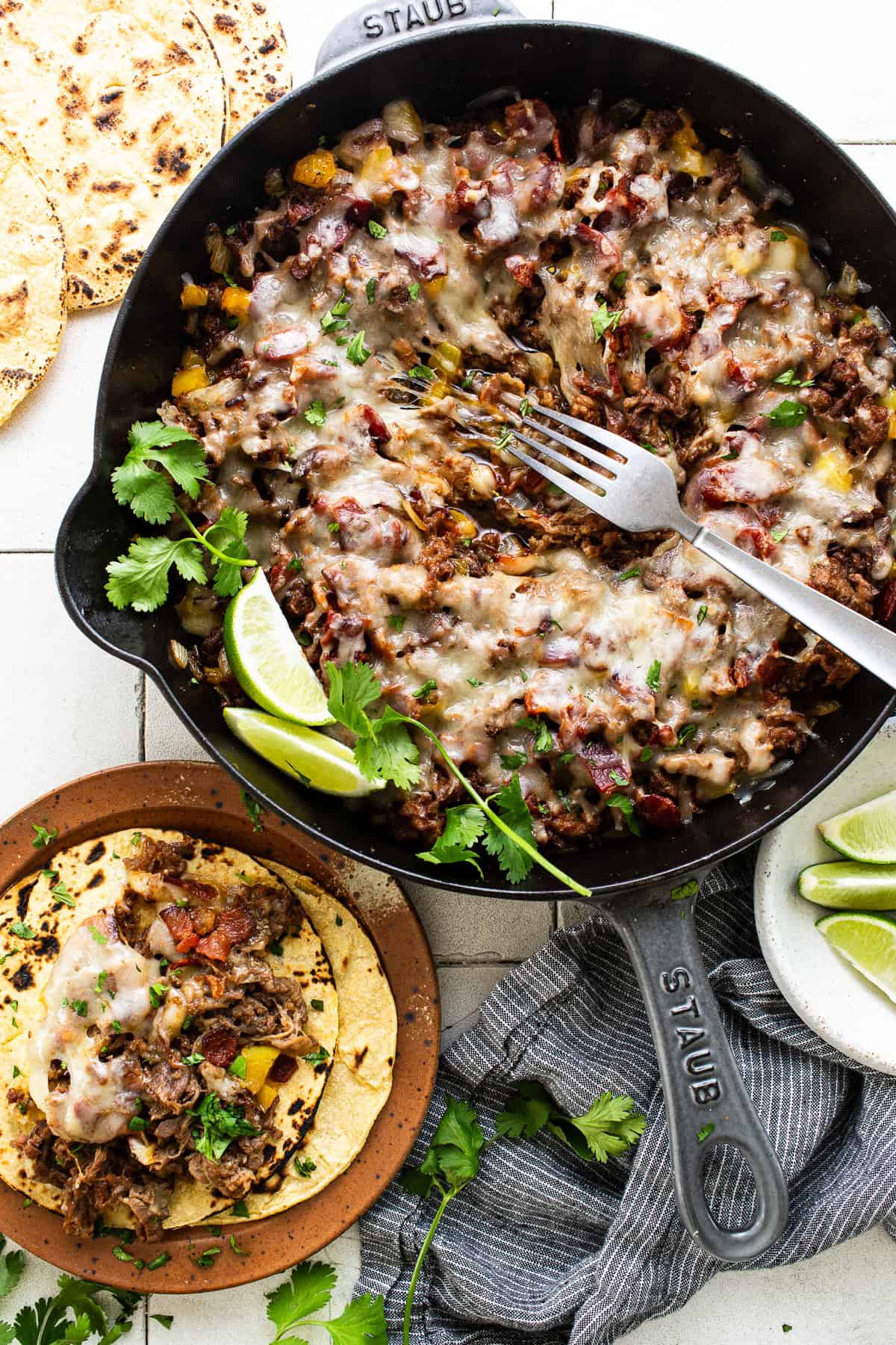 A skillet with the shaved steak, chorizo, peppers, onions, and bacon with melted cheese on top.