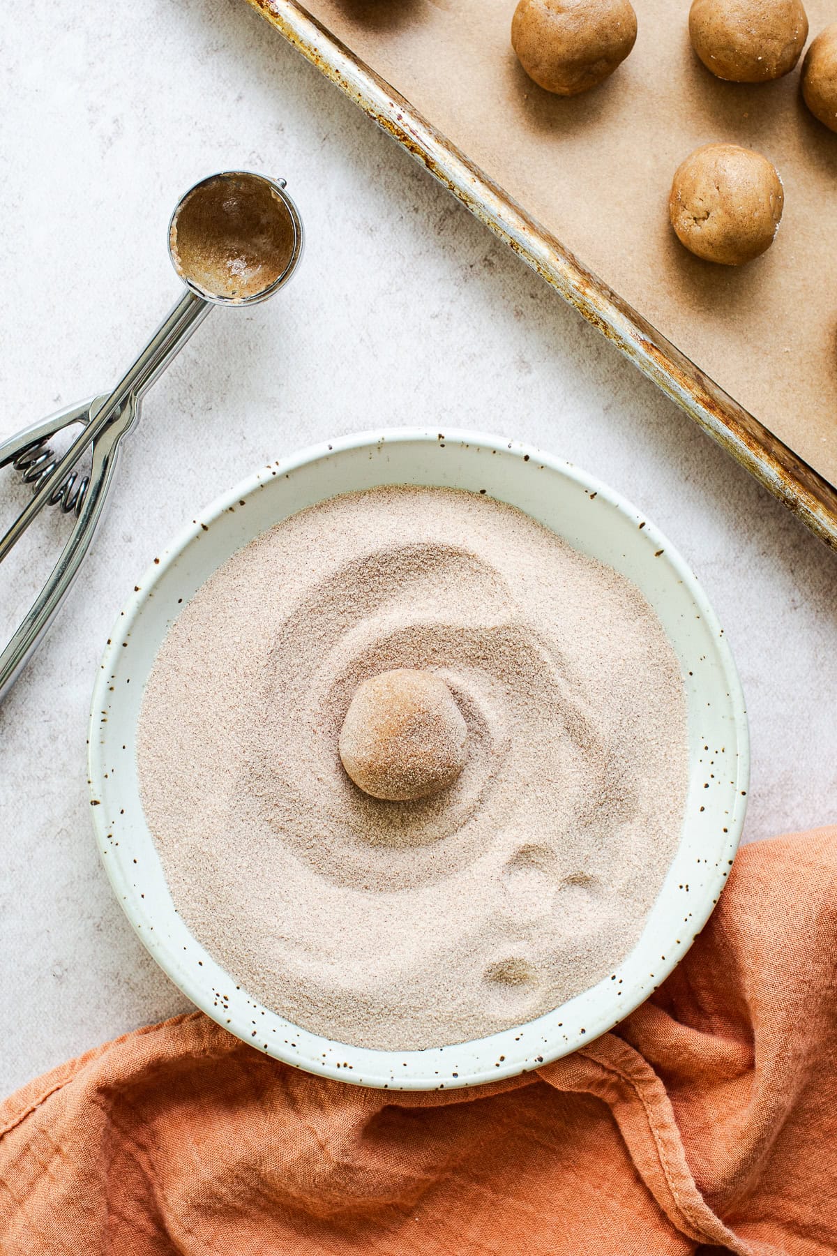 Churro cookie dough being rolled in cinnamon sugar.