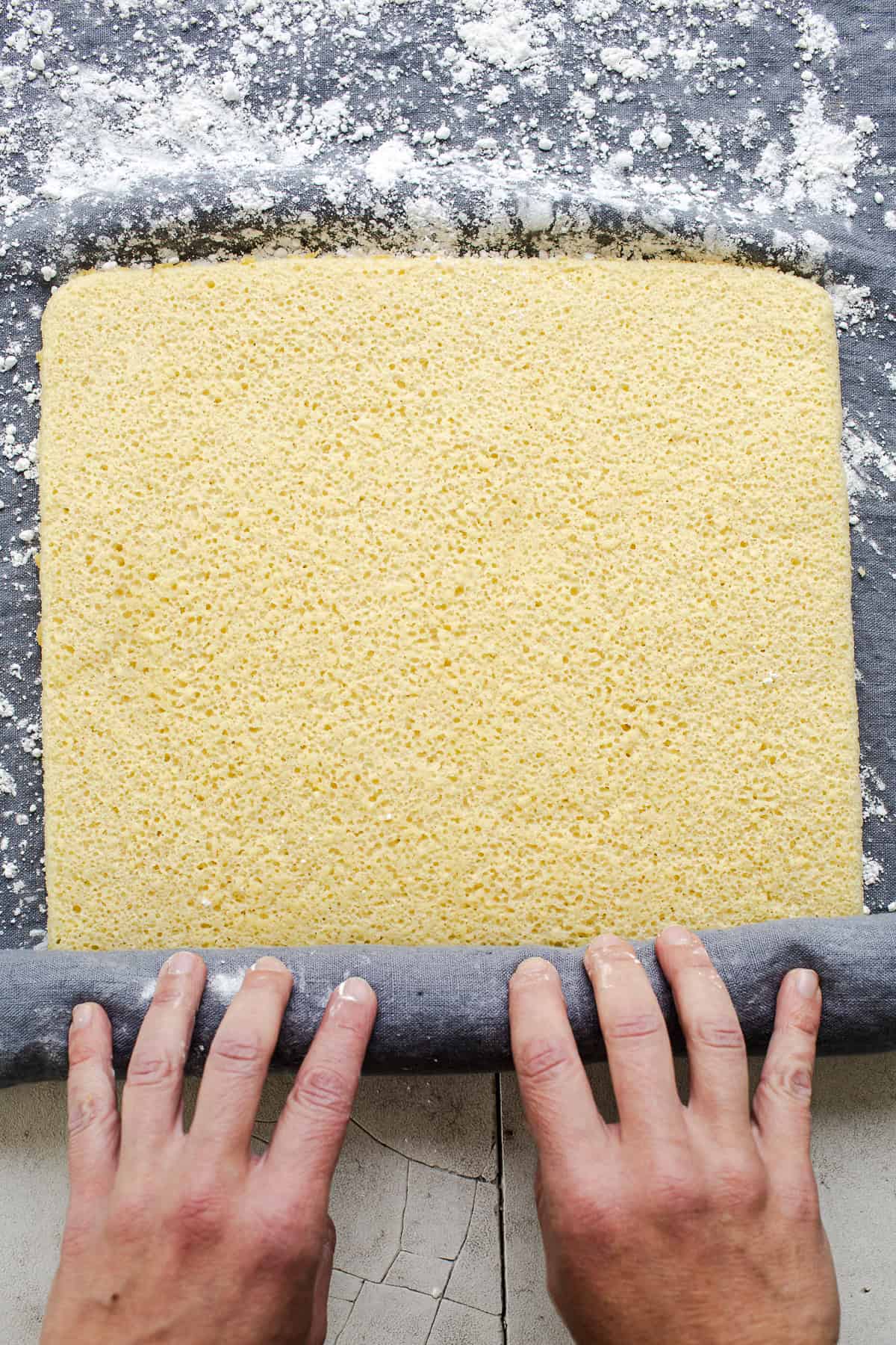 The warm cake being rolled on a towel covered with powdered sugar.