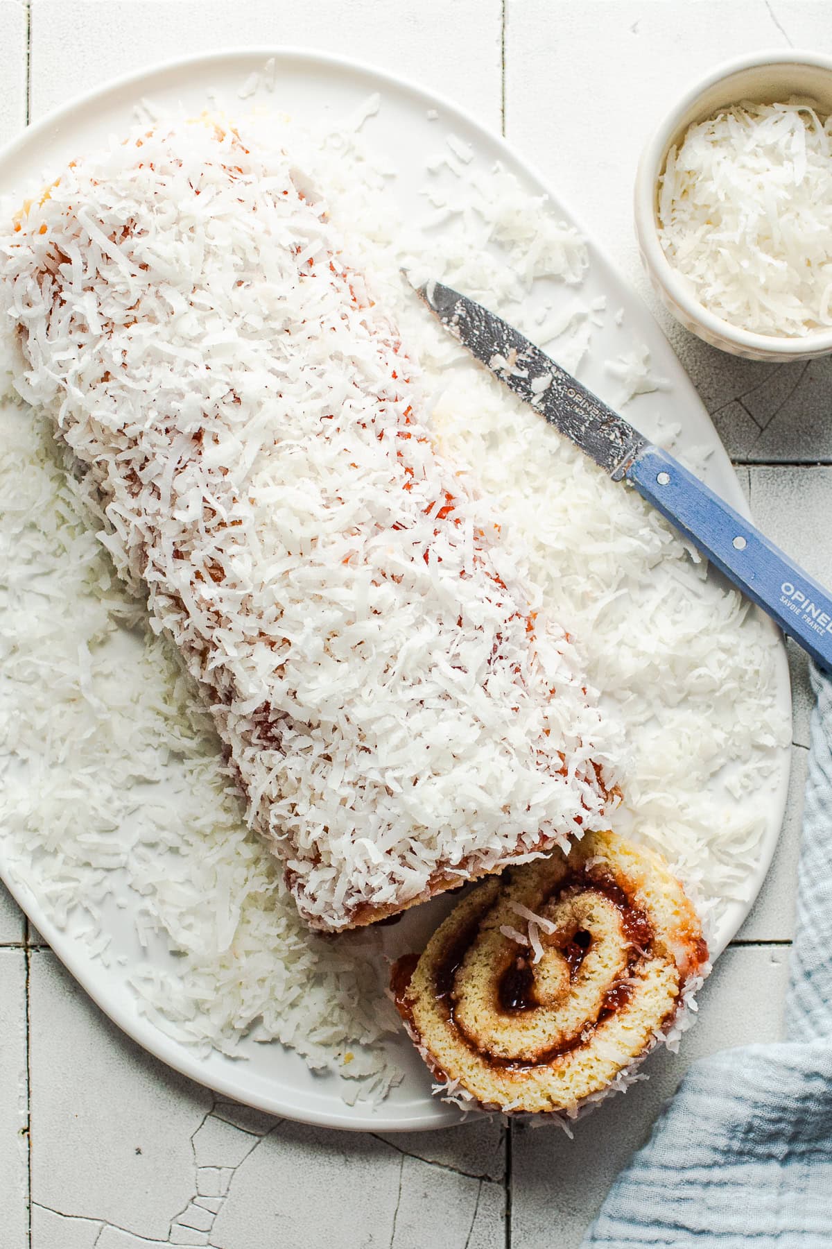 A long niño envuelto roll covered with shredded coconut on a plate.
