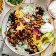 Healthy taco bowl on a table with ground beef, cilantro lime rice, charred skillet corn, pico de gallo, and more toppings.