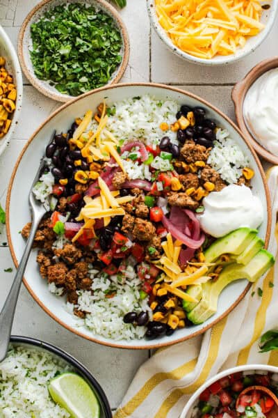 Healthy taco bowl on a table with ground beef, cilantro lime rice, charred skillet corn, pico de gallo, and more toppings.