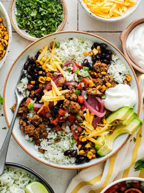 Healthy taco bowl on a table with ground beef, cilantro lime rice, charred skillet corn, pico de gallo, and more toppings.