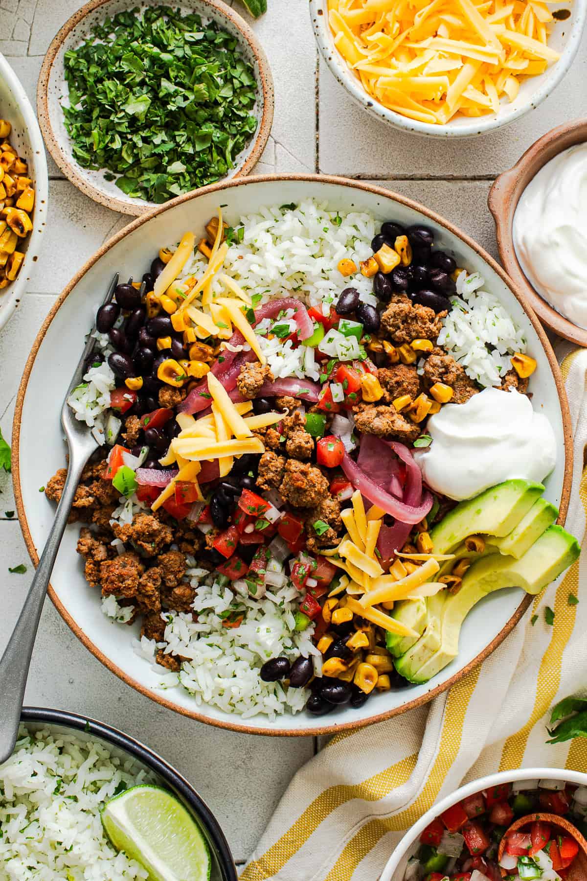 Healthy taco bowl on a table with ground beef, cilantro lime rice, charred skillet corn, pico de gallo, and more toppings.