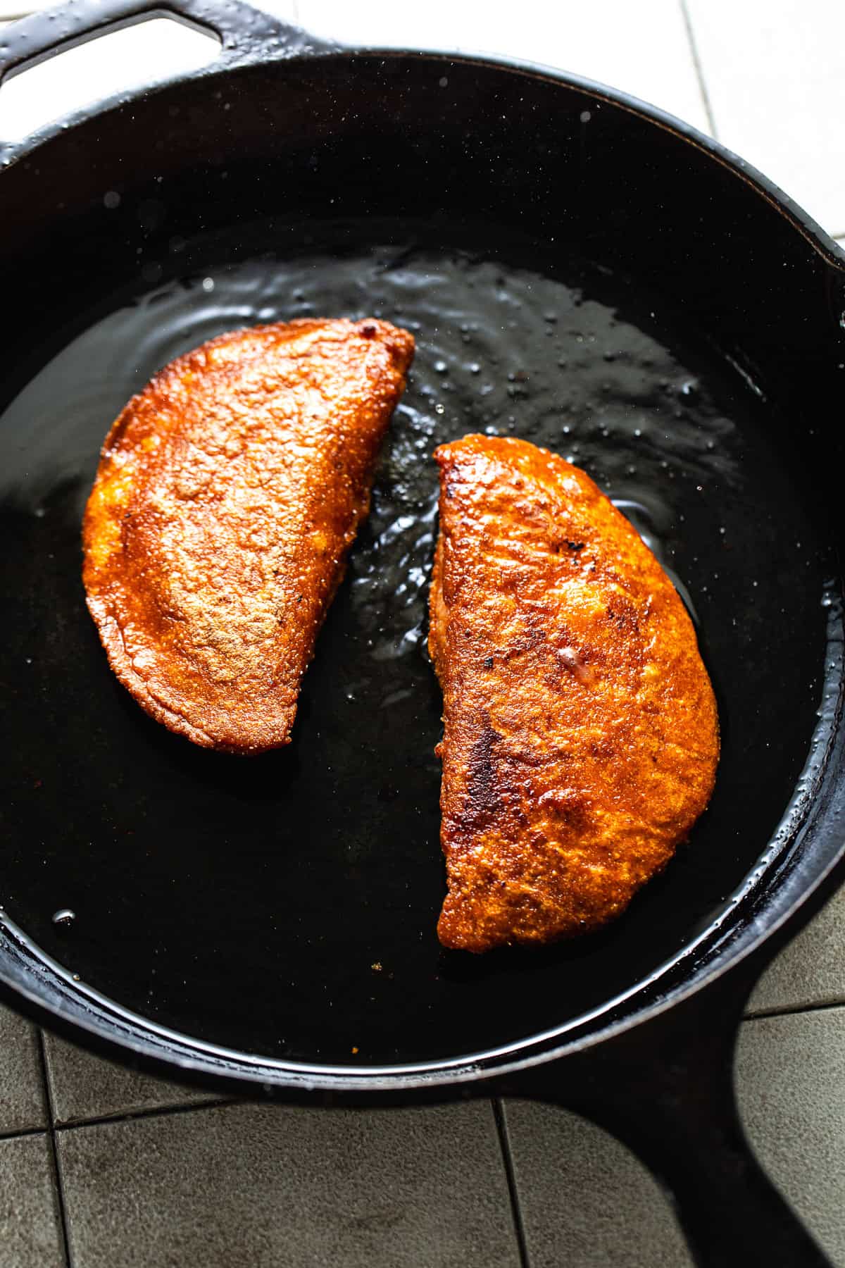 Two enchiladas potosinas shallow frying in a cast iron skillet.