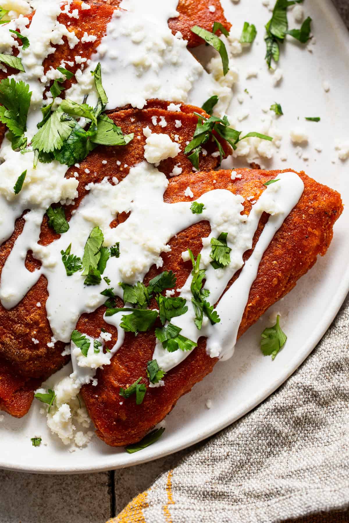 Enchiladas potosinas on a plate drizzled with crema, cotija cheese, and cilantro.