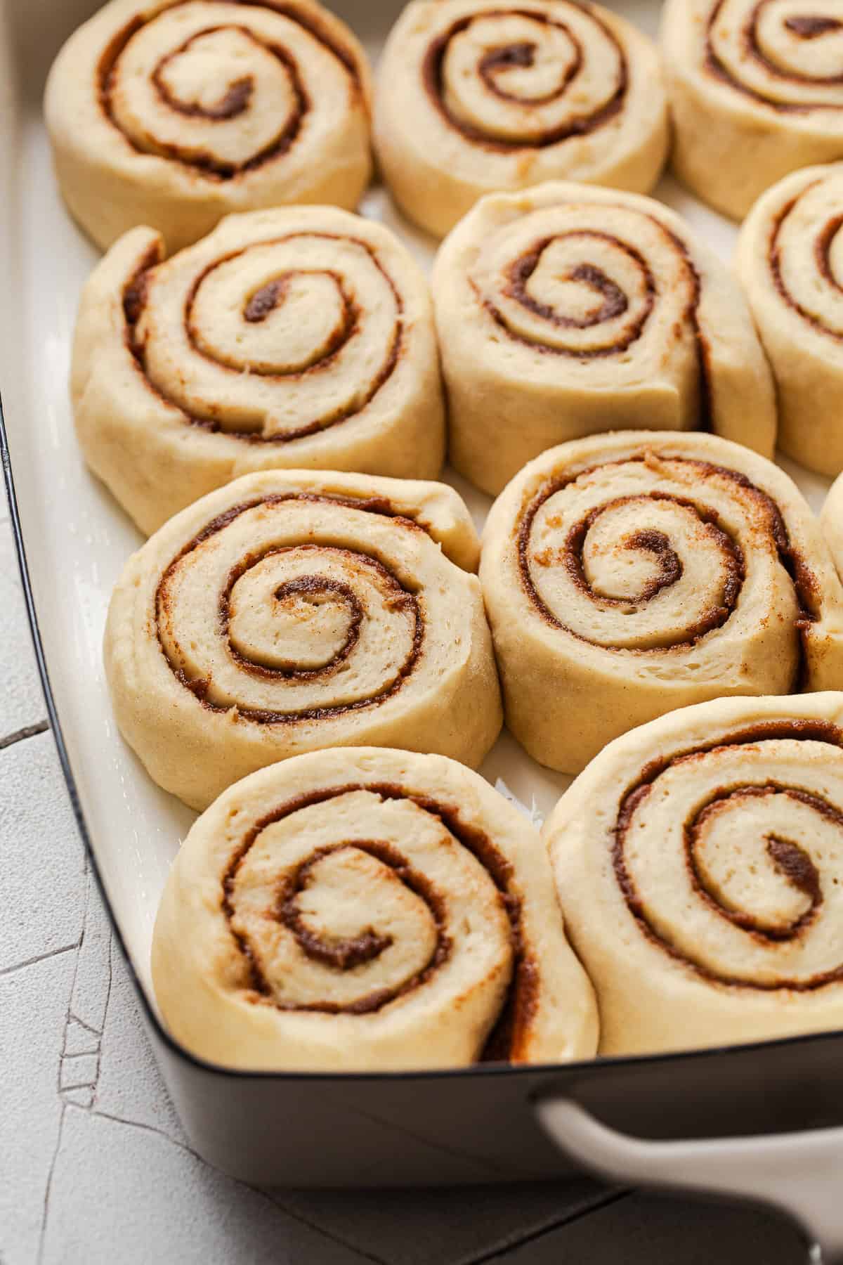 The risen tres leches cinnamon rolls before being baked in a baking dish.
