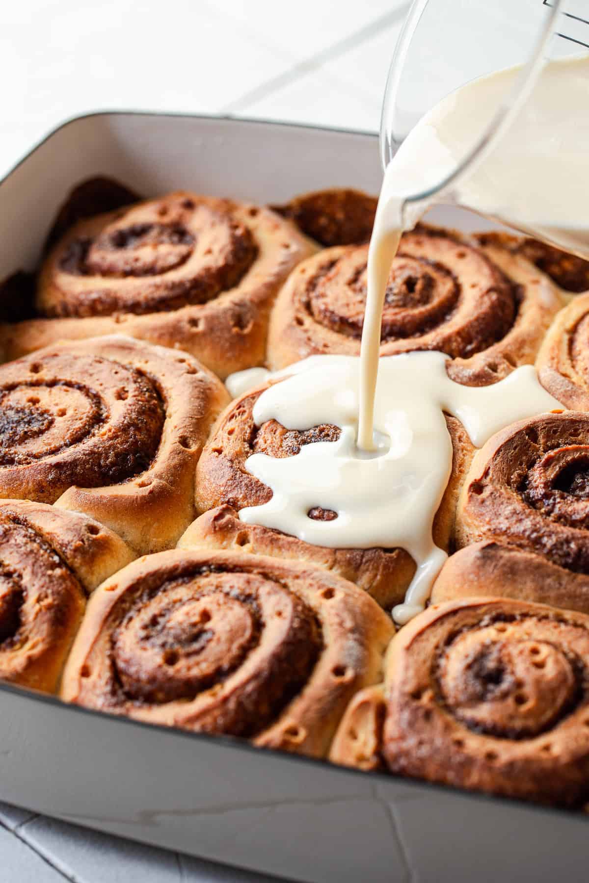 The three milk mixture being poured on top of the baked and poked cinnamon rolls.