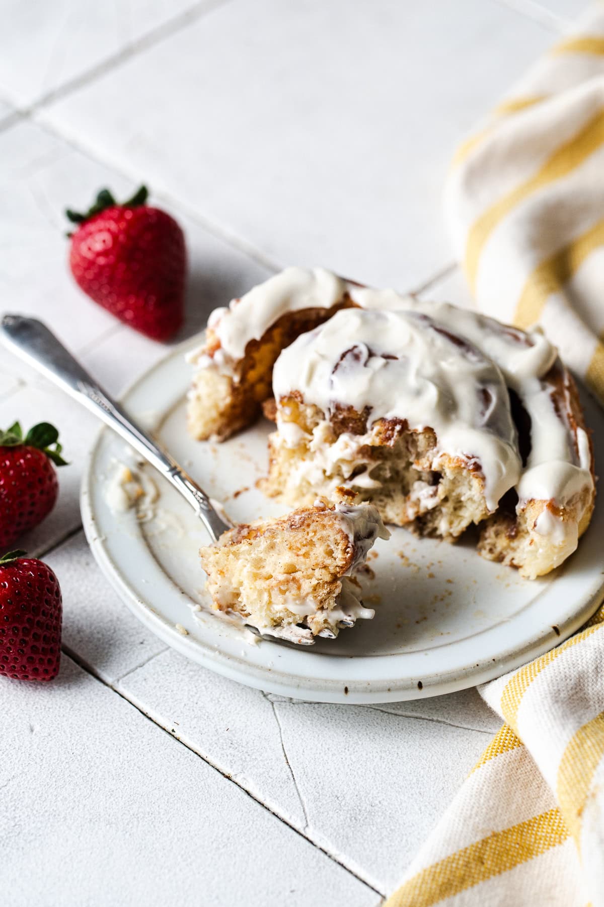 A tres leches cinnamon roll on a plate being eaten with a fork