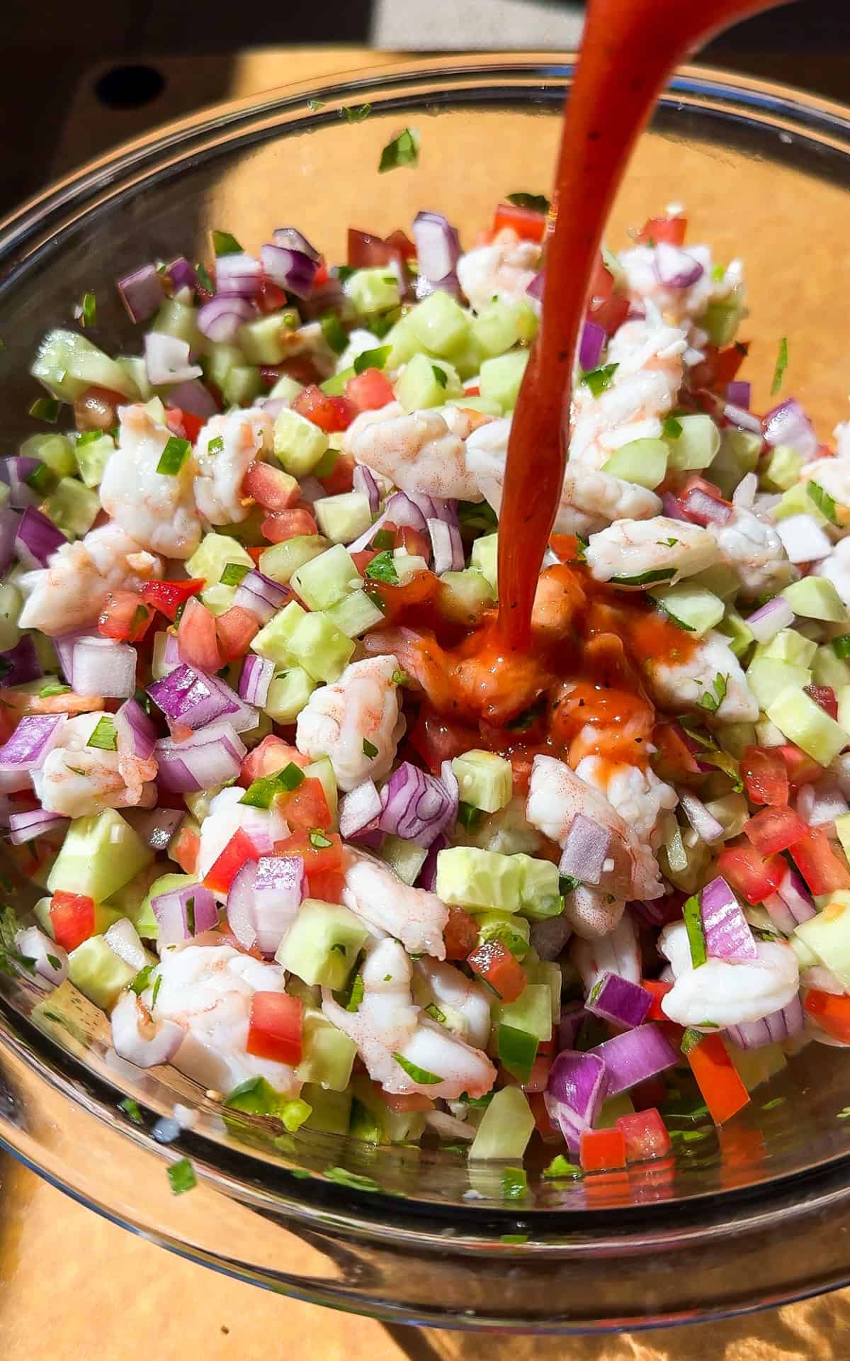 Tomato sauce being poured into a bowl of mexican ceviche before being tossed together to serve.