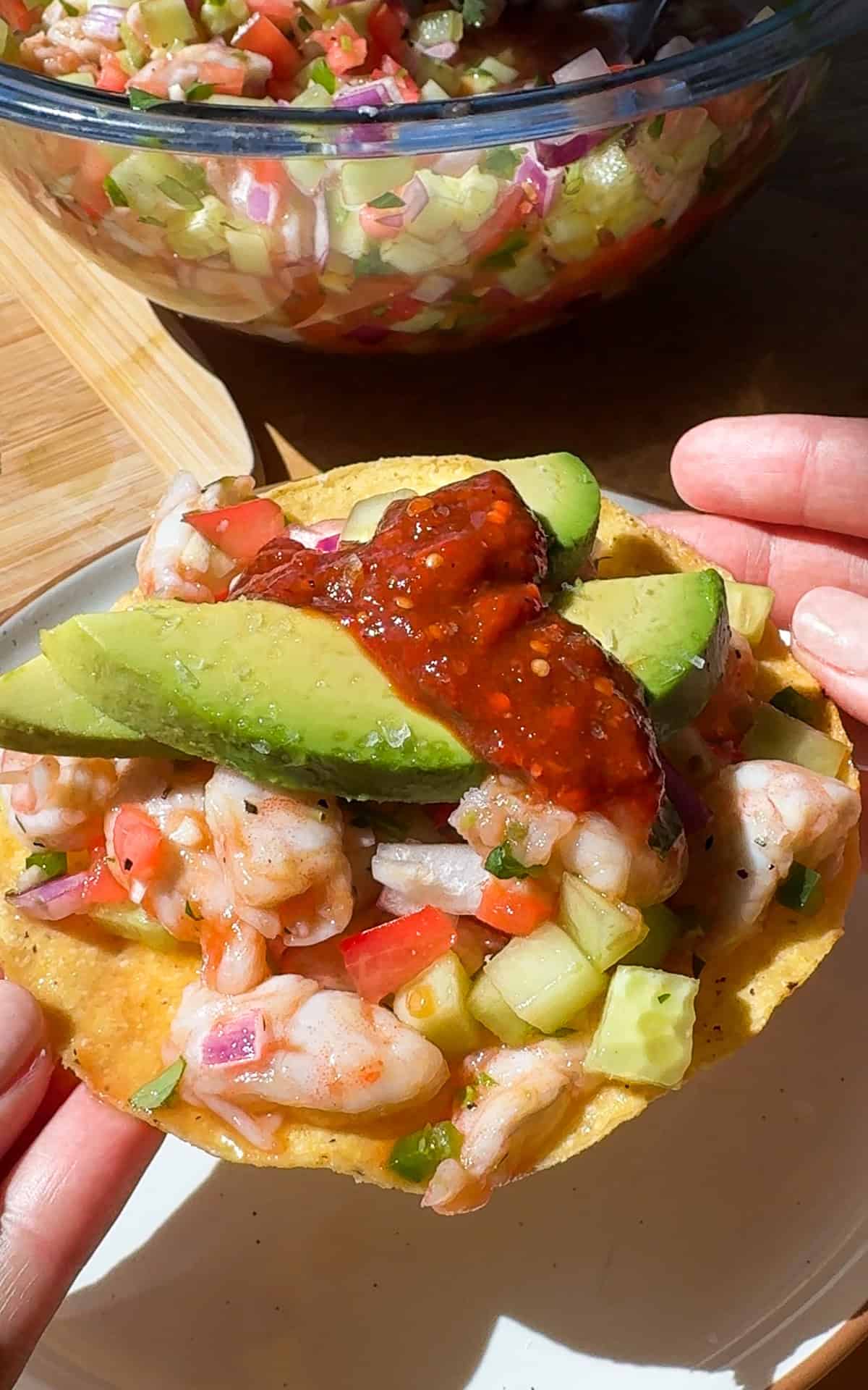 Mexican ceviche on a tostada topped with sliced avocado and salsa.