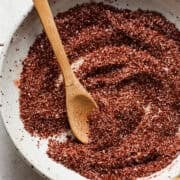 A small bowl of chili lime seasoning with a wooden spoon for sprinkling and serving.