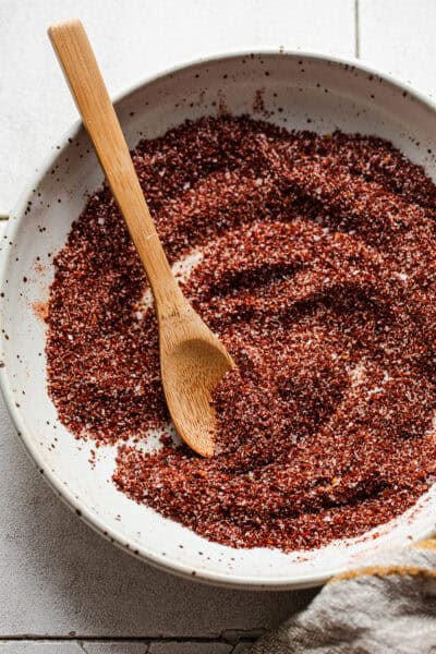 A small bowl of chili lime seasoning with a wooden spoon for sprinkling and serving.