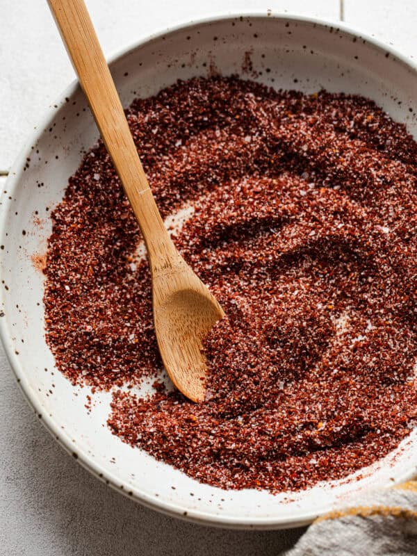 A small bowl of chili lime seasoning with a wooden spoon for sprinkling and serving.