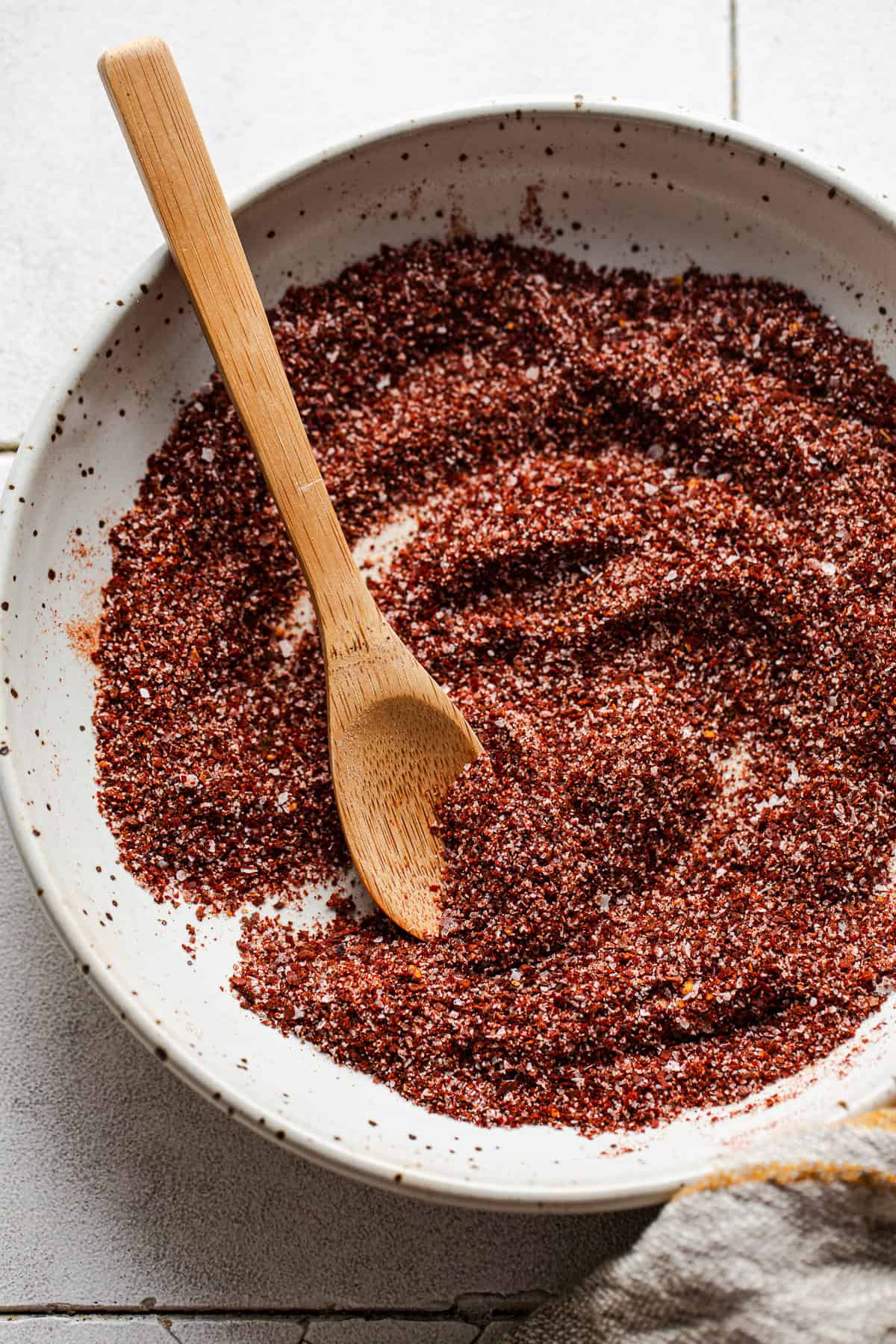 A small bowl of chili lime seasoning with a wooden spoon for sprinkling and serving.