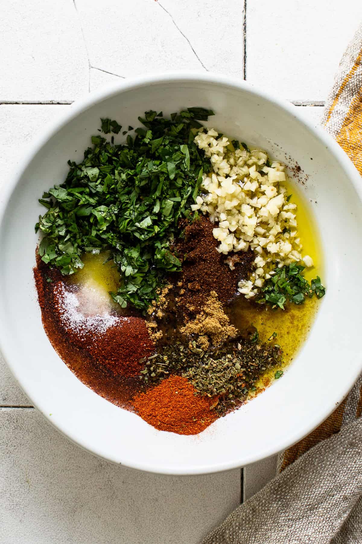 A bowl with all of the ingredients to make Mexican chicken marinade before being mixed together - dry seasonings and spices, garlic, chopped cilantro, olive oil, and lime juice.