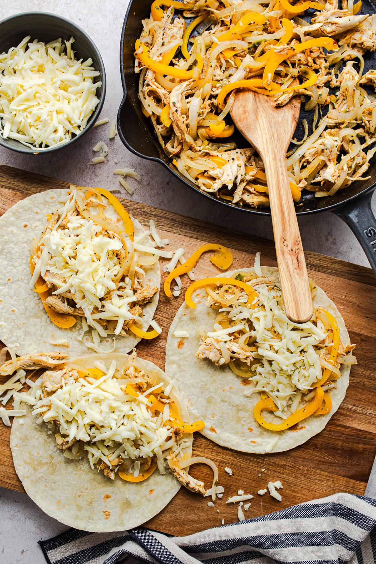 Rotisserie chicken tacos being assembled with the shredded chicken filling and shredded cheese on flour tortillas.