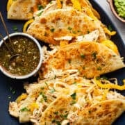 A plate of crispy golden rotisserie chicken tacos served with a roasted tomatillo salsa.