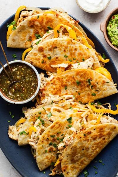 A plate of crispy golden rotisserie chicken tacos served with a roasted tomatillo salsa.