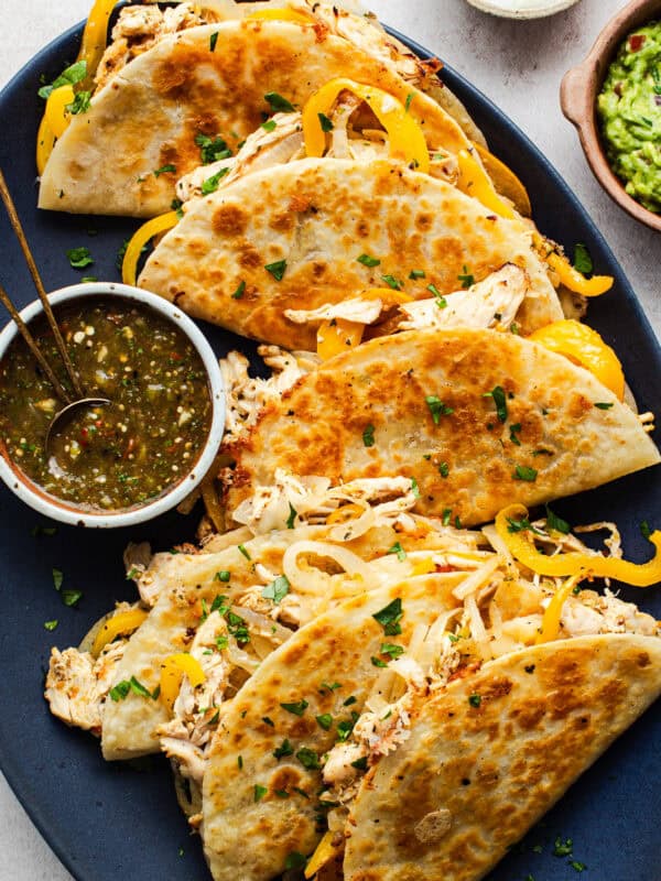 A plate of crispy golden rotisserie chicken tacos served with a roasted tomatillo salsa.