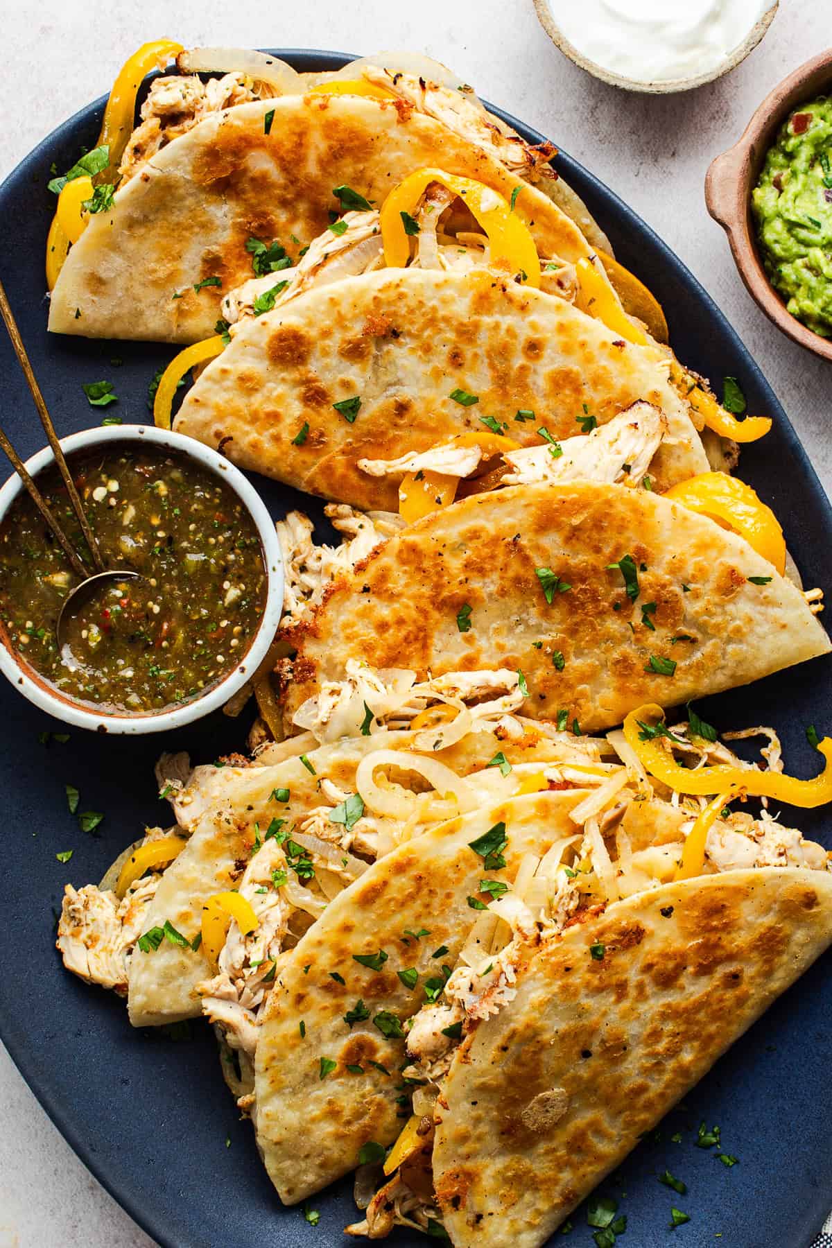 A plate of crispy golden rotisserie chicken tacos served with a roasted tomatillo salsa.