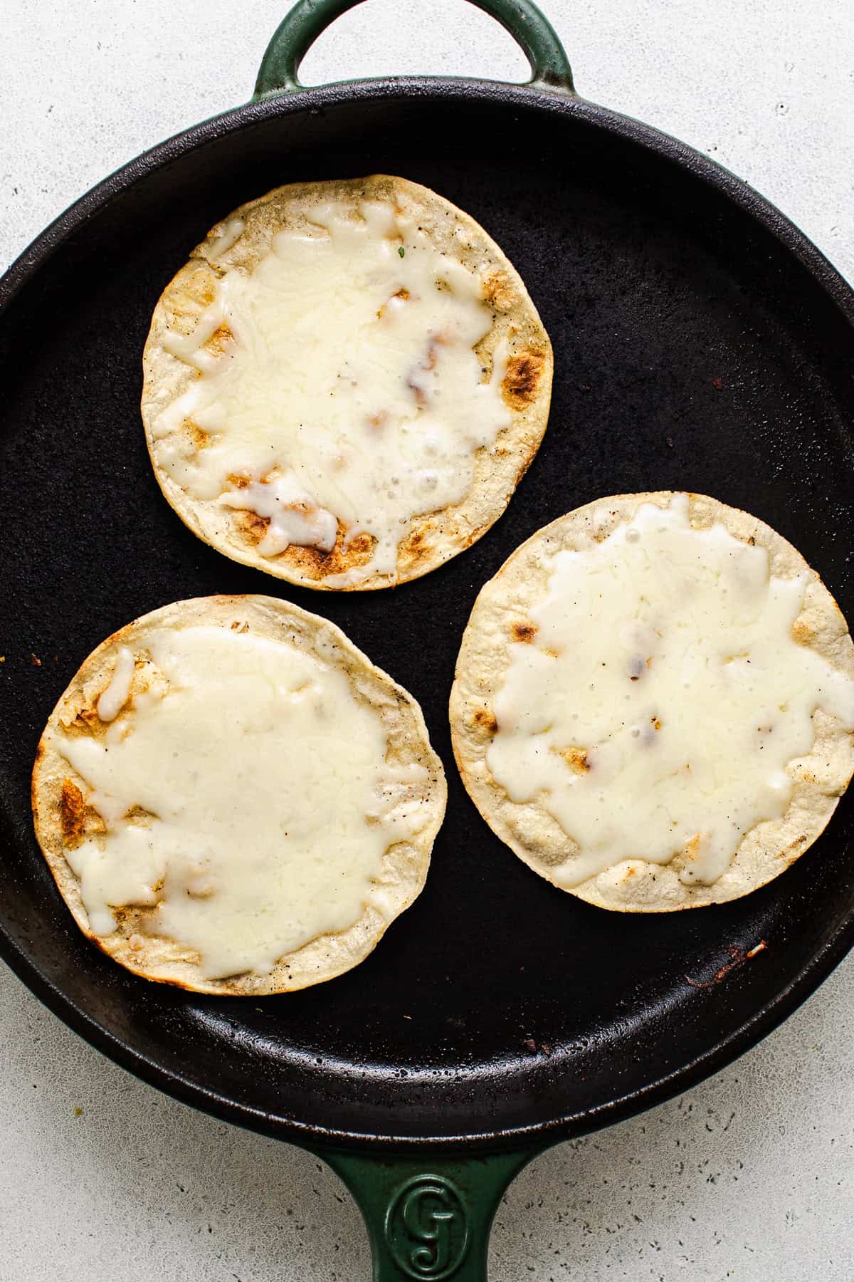 Melted cheese on the crisped up corn tortillas in a skillet for vampiro tacos.