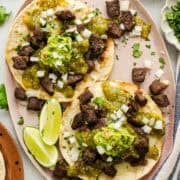 A plate of vampiro tacos topped with carne asada, salsa verde, and guacamole.