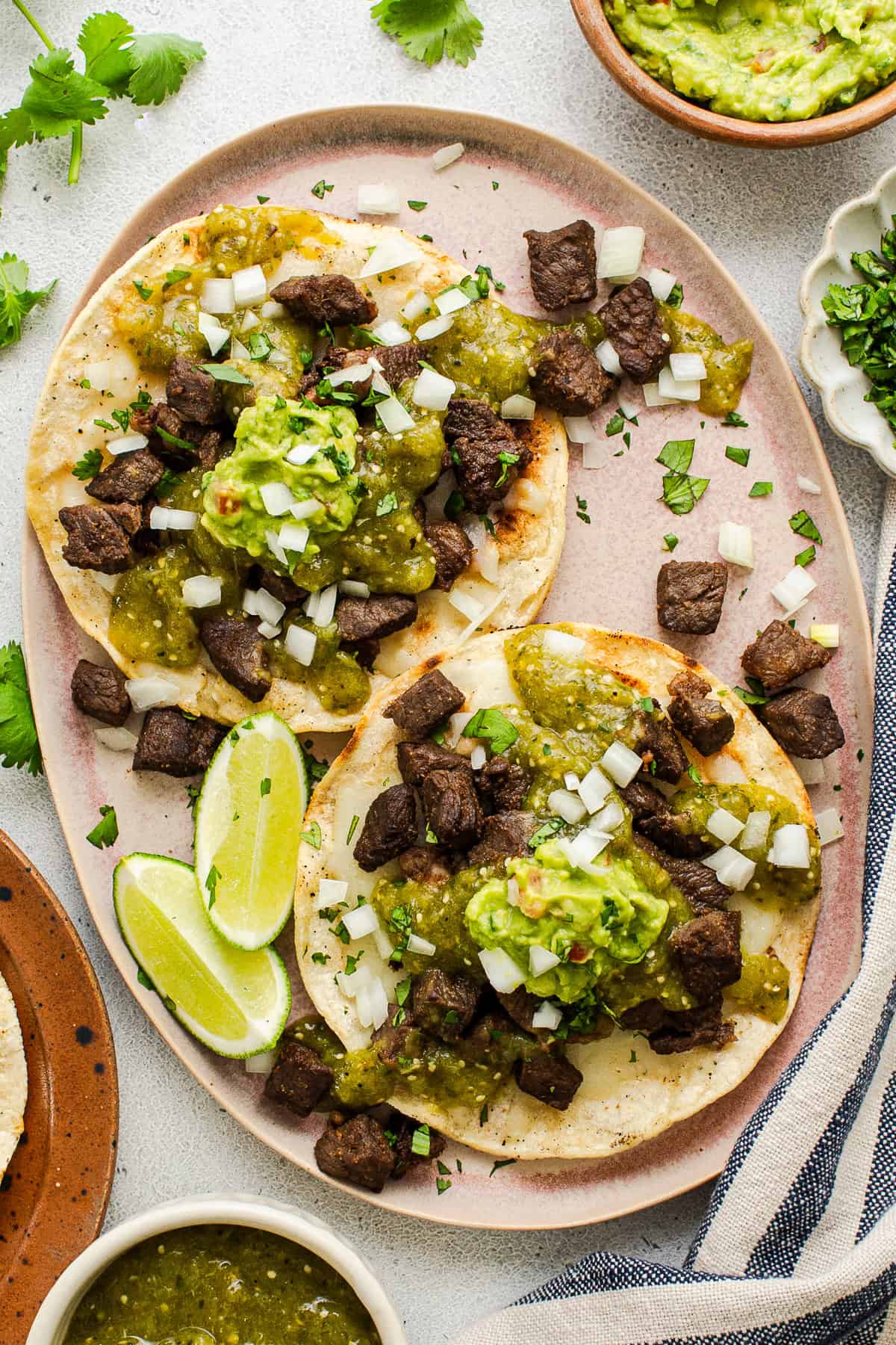 A plate of vampiro tacos topped with carne asada, salsa verde, and guacamole.