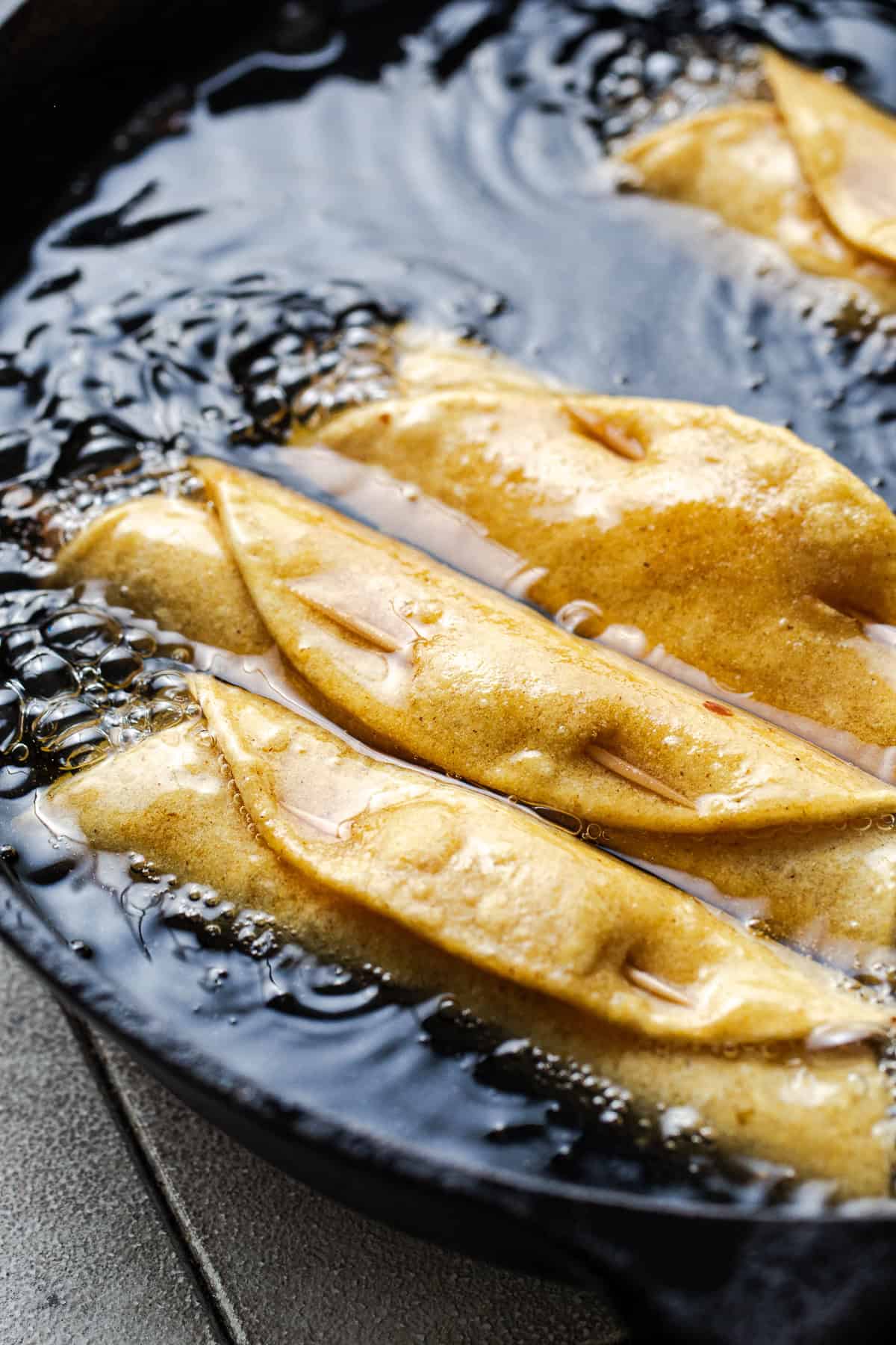 Flautas frying in a skillet of oil to make flautas ahogadas.