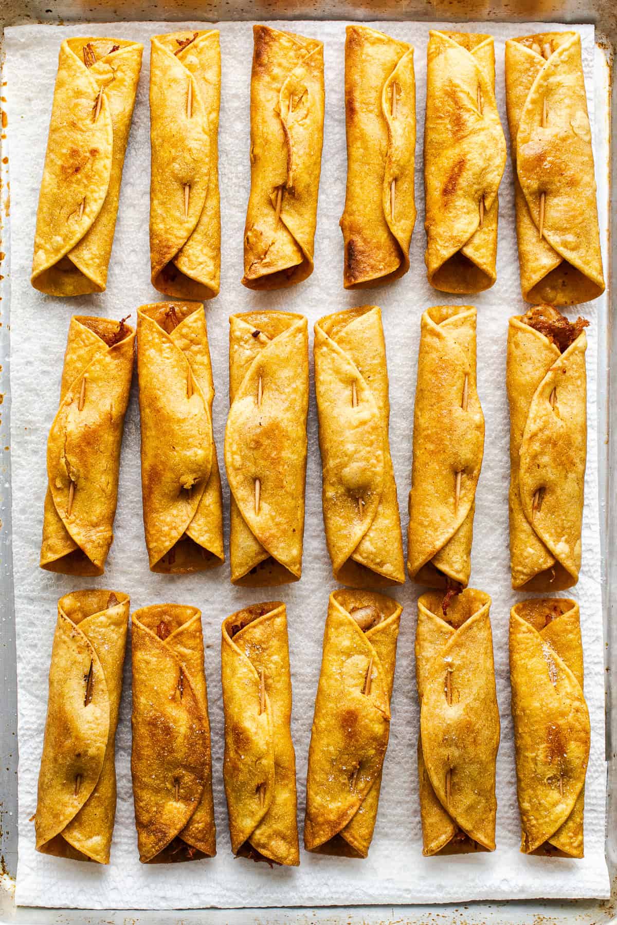 Flautas on a sheet pan lined with paper towels to help drain off excess oil.