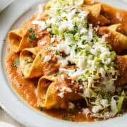 A plate of flautas ahogadas drowned in a salsa roja with shredded lettuce, crema, cotija cheese, and cilantro.