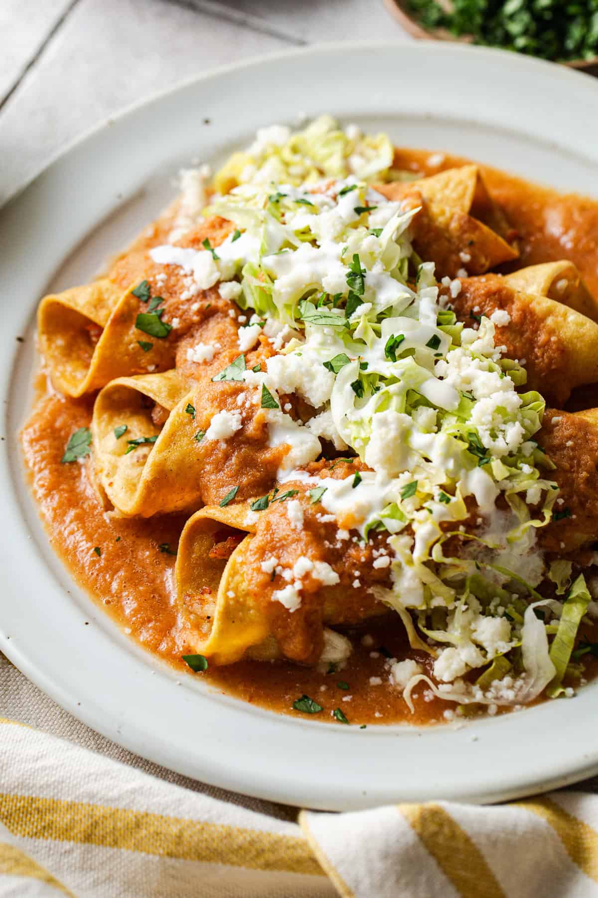 A plate of flautas ahogadas drowned in a salsa roja with shredded lettuce, crema, cotija cheese, and cilantro.