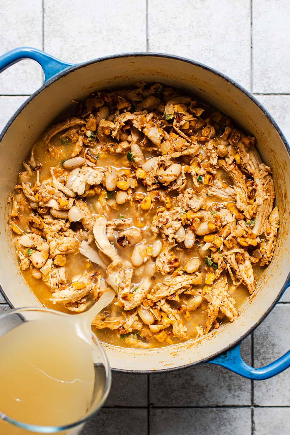 Broth being poured into a pot of Mexican street corn white chicken chili during the cooking process.