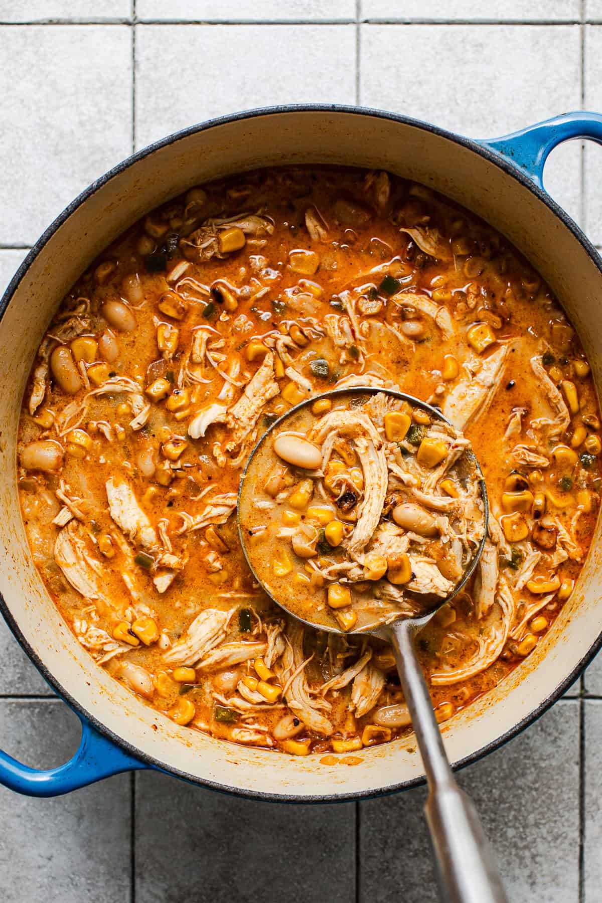 A ladle grabbing some Mexican street corn chicken chili from a large Dutch oven.