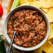 A bowl of roasted salsa made with fresh tomatoes on a platter next to tortilla chips.