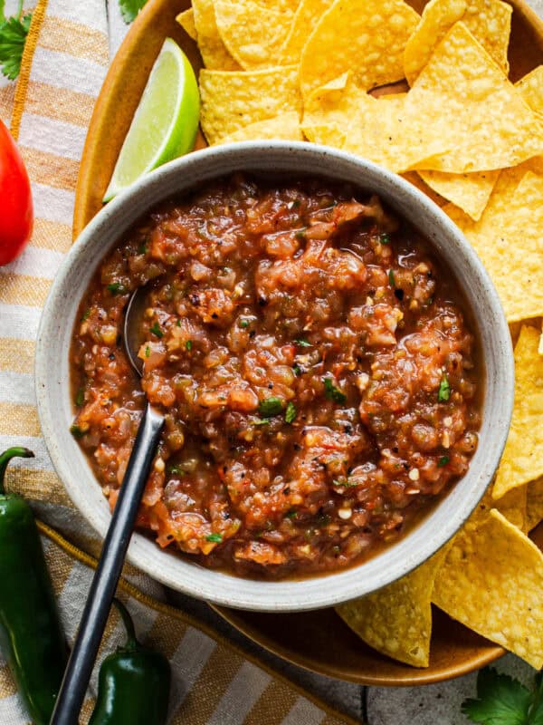 A bowl of roasted salsa made with fresh tomatoes on a platter next to tortilla chips.