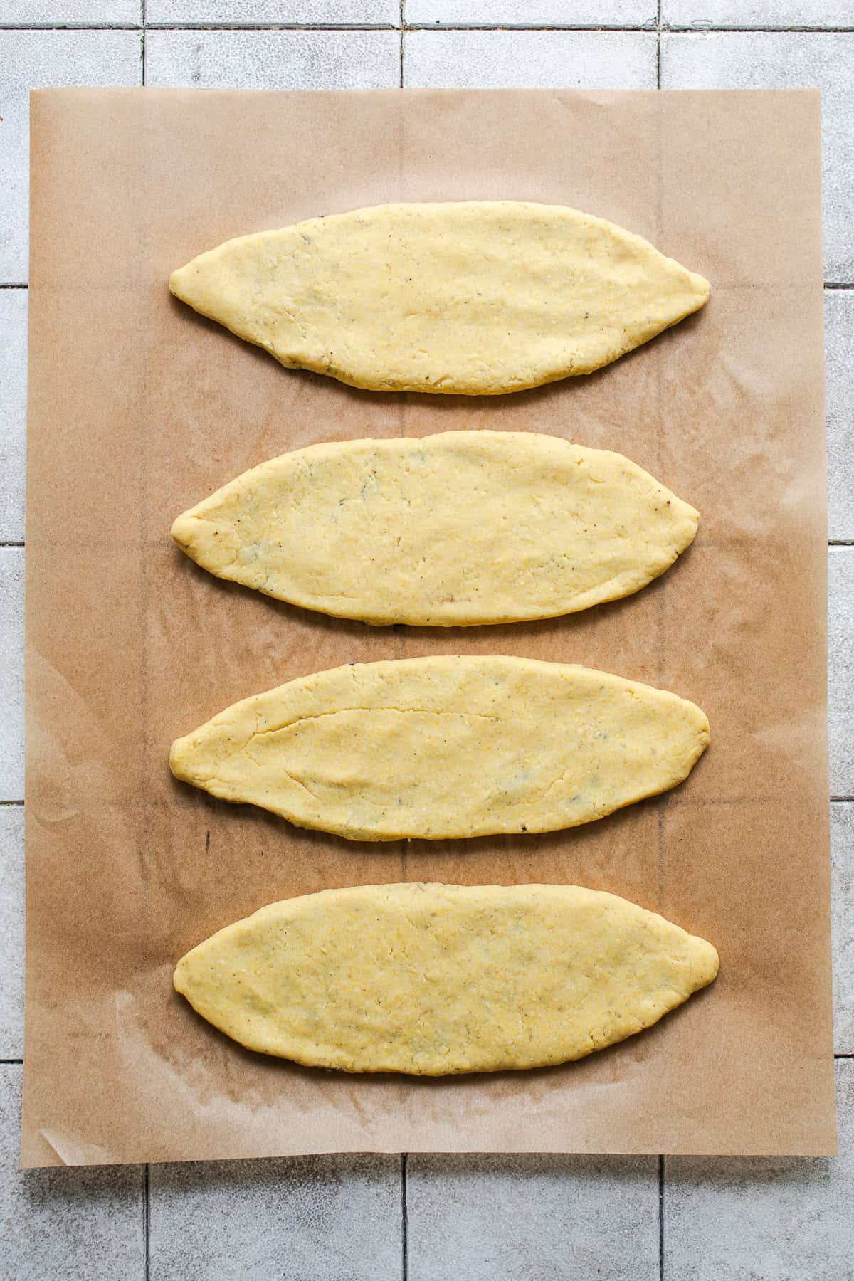 Four uncooked and shaped tlacoyos on parchment paper.