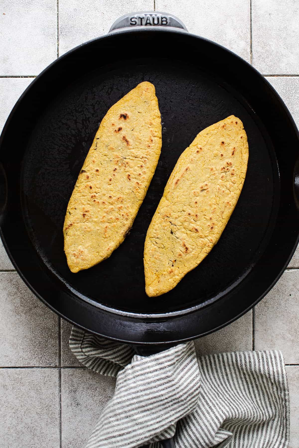 Two tlacoyos cooking in a dry cast iron skillet.
