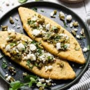 Tlacoyos on a plate topped with cooked nopales, cilantro, and queso fresco.