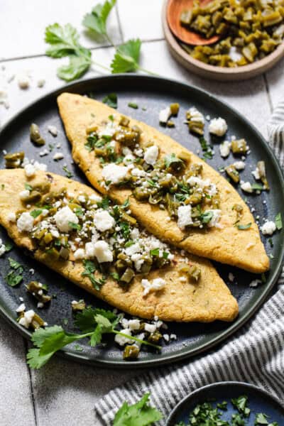 Tlacoyos on a plate topped with cooked nopales, cilantro, and queso fresco.