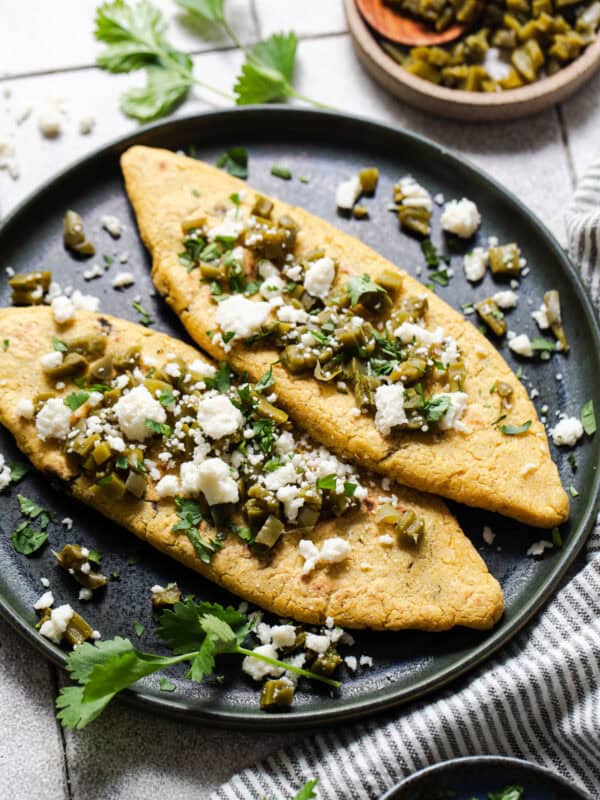 Tlacoyos on a plate topped with cooked nopales, cilantro, and queso fresco.