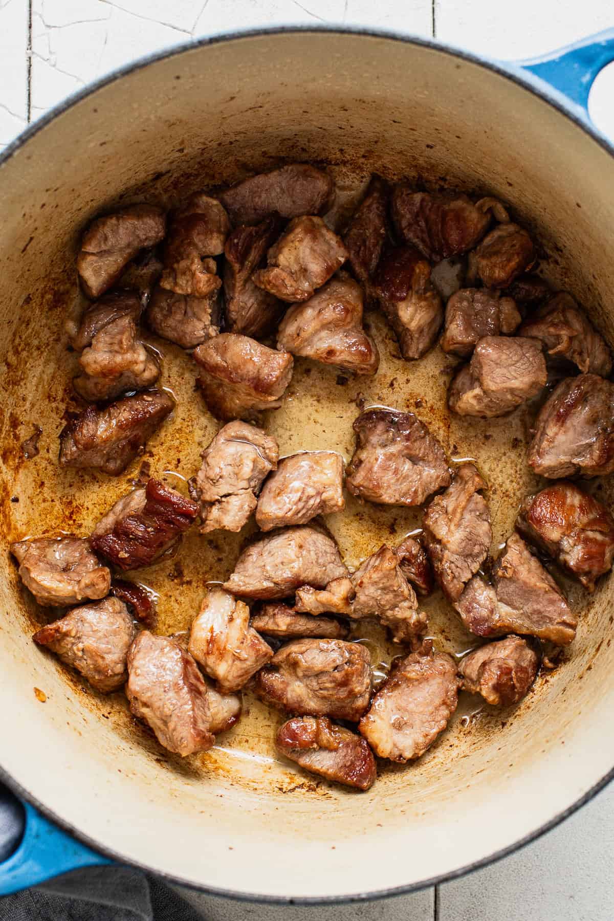Seared pork shoulder bite-sized pieces in a large Dutch oven